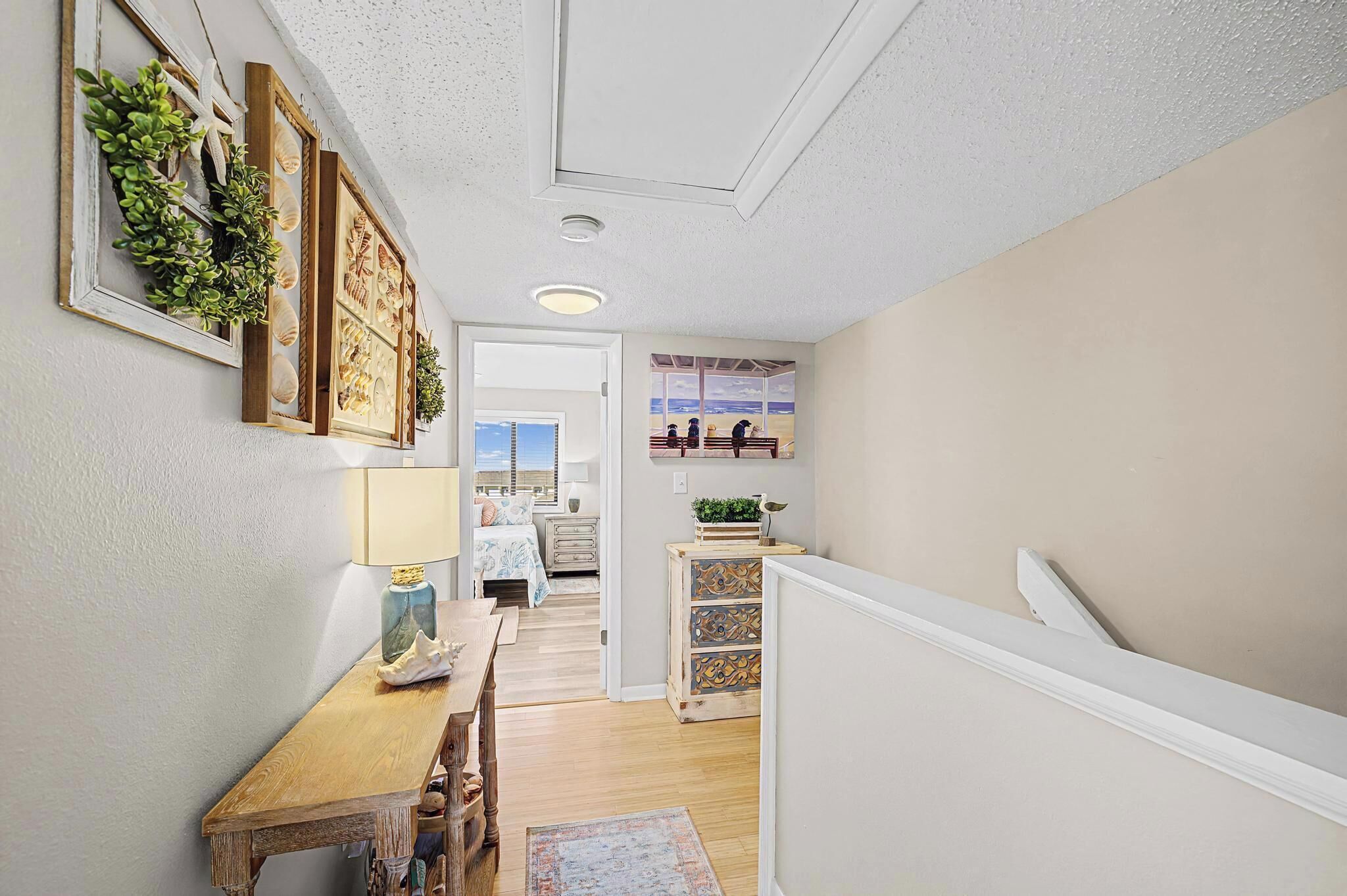 A hallway with a wooden bench, a table, and a view of a beach through a window.