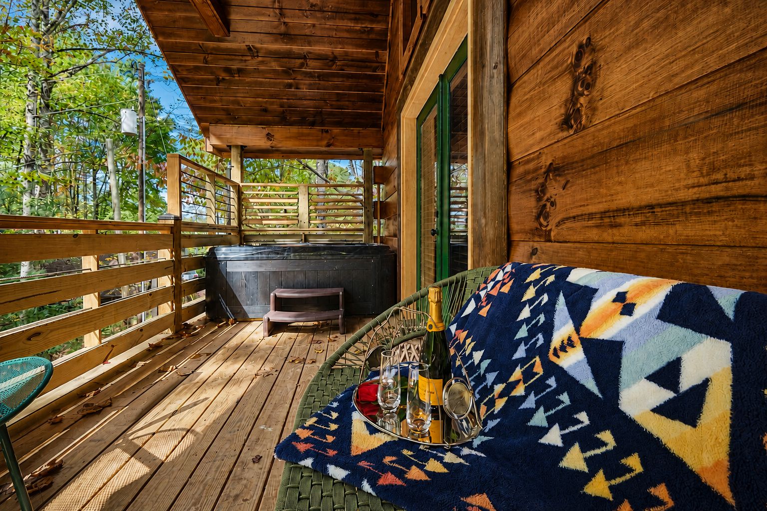 Een houten terras met een overdekte zithoek, een jacuzzi en uitzicht op bomen.