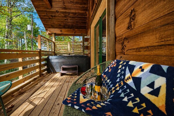 A wooden deck with a covered seating area, a hot tub, and a view of trees.