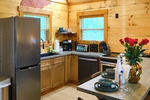 A wooden cabin kitchen with a refrigerator, microwave, toaster, and a dining area with plates and a vase of flowers.