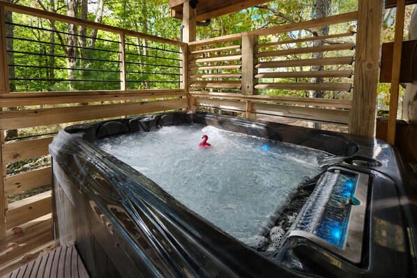 A hot tub with a pink flamingo float, surrounded by wooden railings and a natural backdrop.