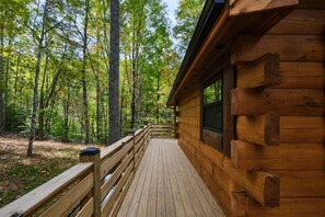 A wooden cabin with a deck, surrounded by a forest. - Fall Hidden Gem | Fireside Jacuzzi + Hot Tub (Sevierville)