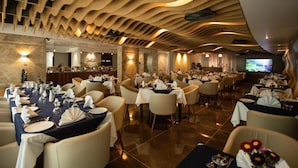 Un restaurant spacieux doté de nombreuses tables, aménagé pour accueillir les clients, et qui se distingue par un plafond aux lignes ondulantes originales et un éclairage d’ambiance chaleureux.