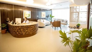 Un hall d’accueil moderne, avec un comptoir en bois, un réceptionniste et un espace détente comprenant des canapés et des fauteuils blancs.