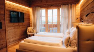 A wooden cabin-style room with a bed, a chair, a TV mounted on the wall, and a window with curtains.
