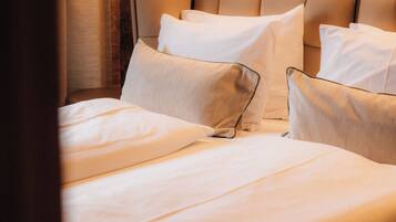 A neatly made bed with white linens and pillows, a wooden headboard, and a wall-mounted light fixture.