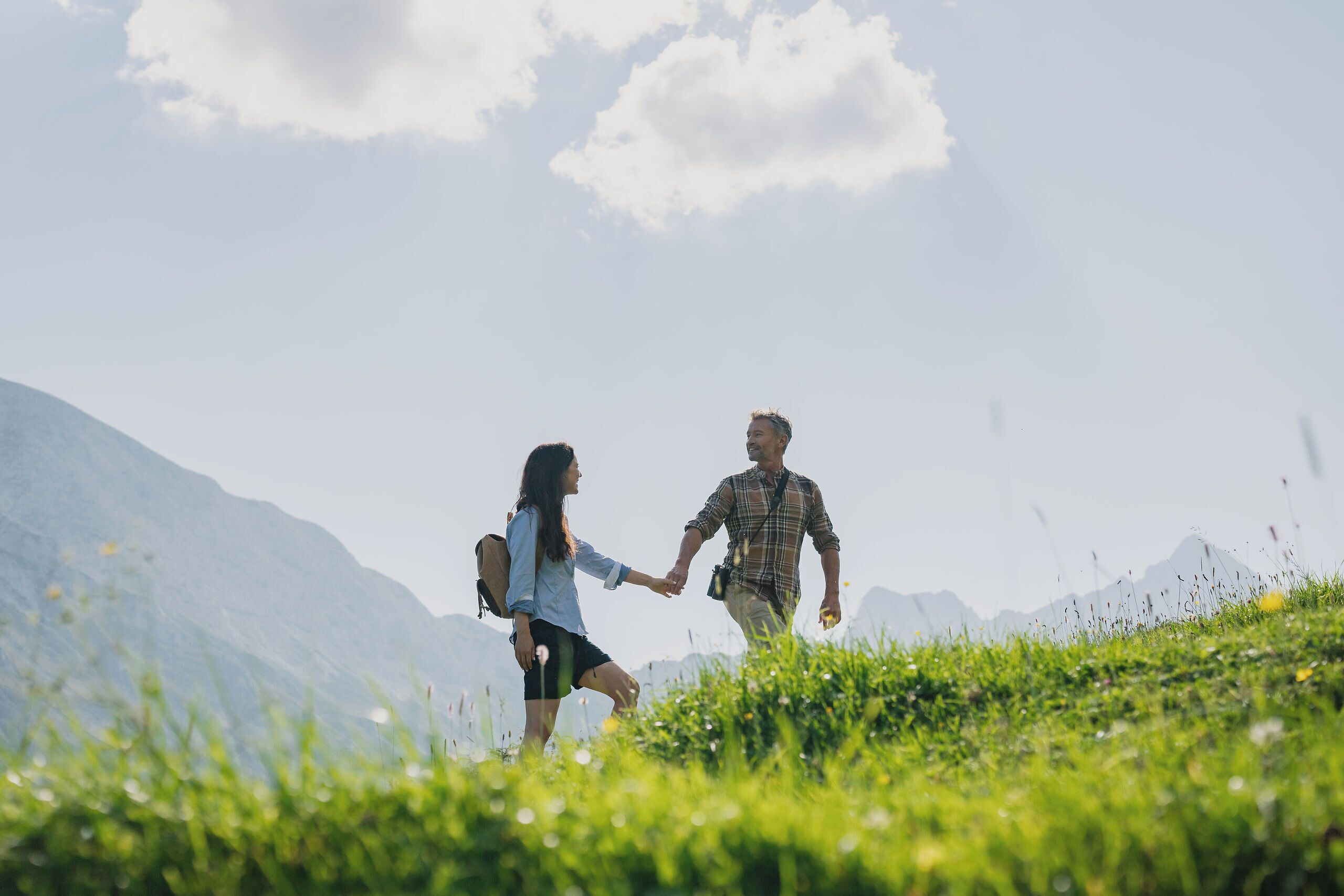 Two people walking on a grassy hill with mountains in the background.