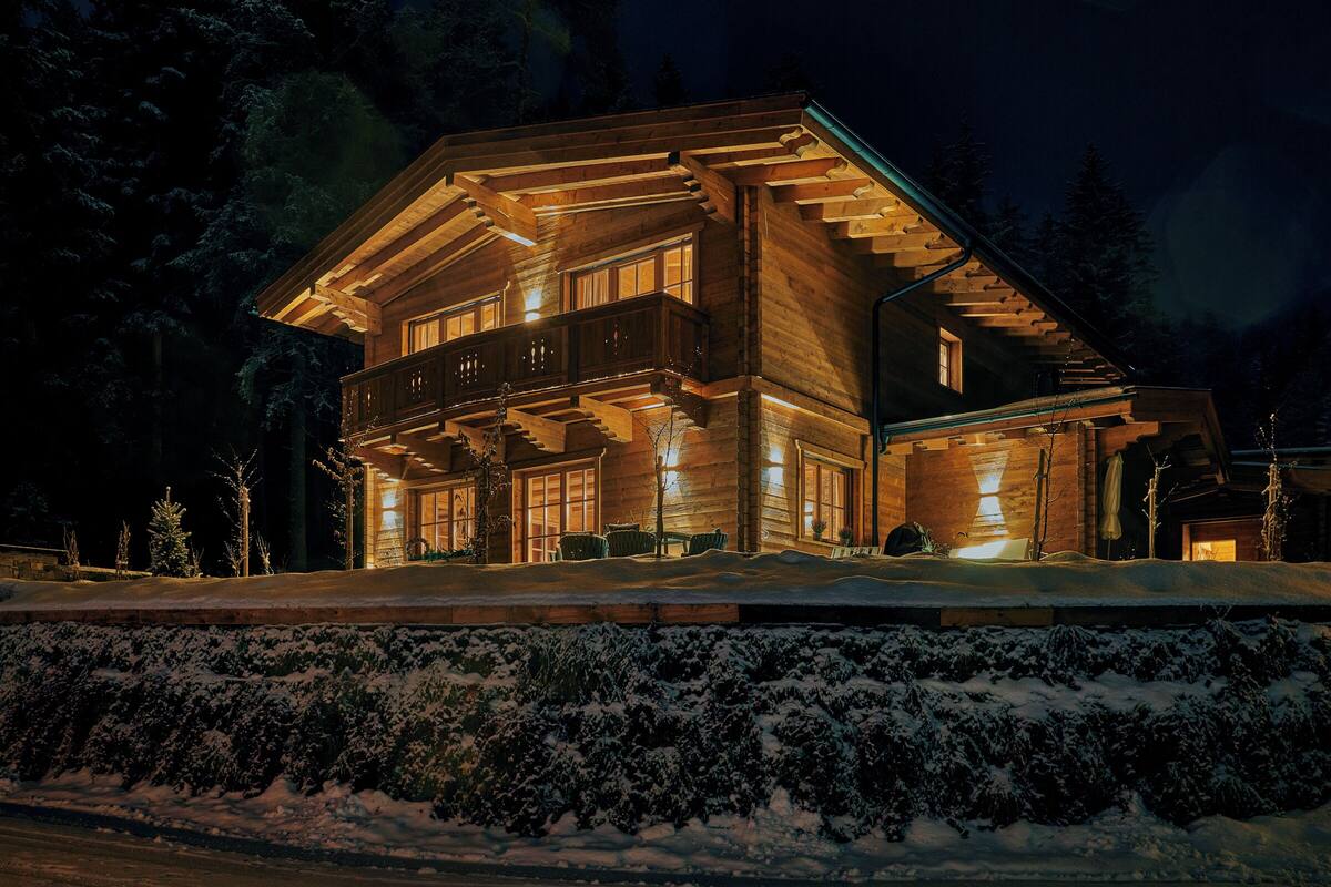 A large log cabin with a balcony, surrounded by snow and trees.