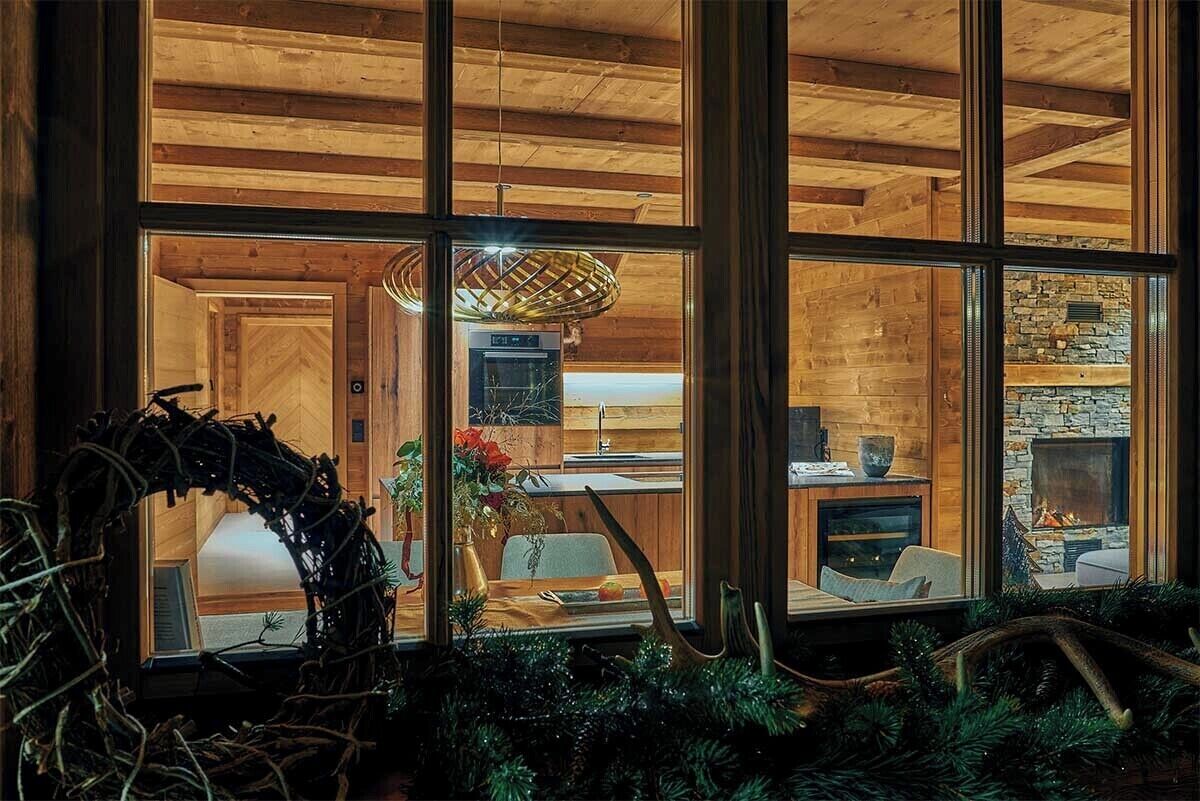 Una habitación con un ventanal grande, vigas de techo de madera, chimenea y un comedor con mesa y sillas.