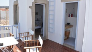 Eine Holzterrasse mit Tisch und Stühlen, einer Leiter und einer Tür zu einem Raum mit einem Bett und einem Badezimmer.
