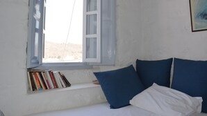 Ein Schlafzimmer mit einem Bett, einem Fenster mit geöffneten Rollläden und einem Regal mit Büchern.