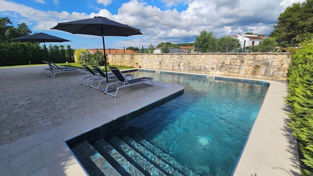 A swimming pool with lounge chairs and umbrellas, surrounded by stone walls and greenery. - Apartments with Shared Pool Casa Bianca (Kanfanar)