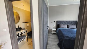Un dormitorio con cama, mesita de noche y baño con lavamanos y espejo.