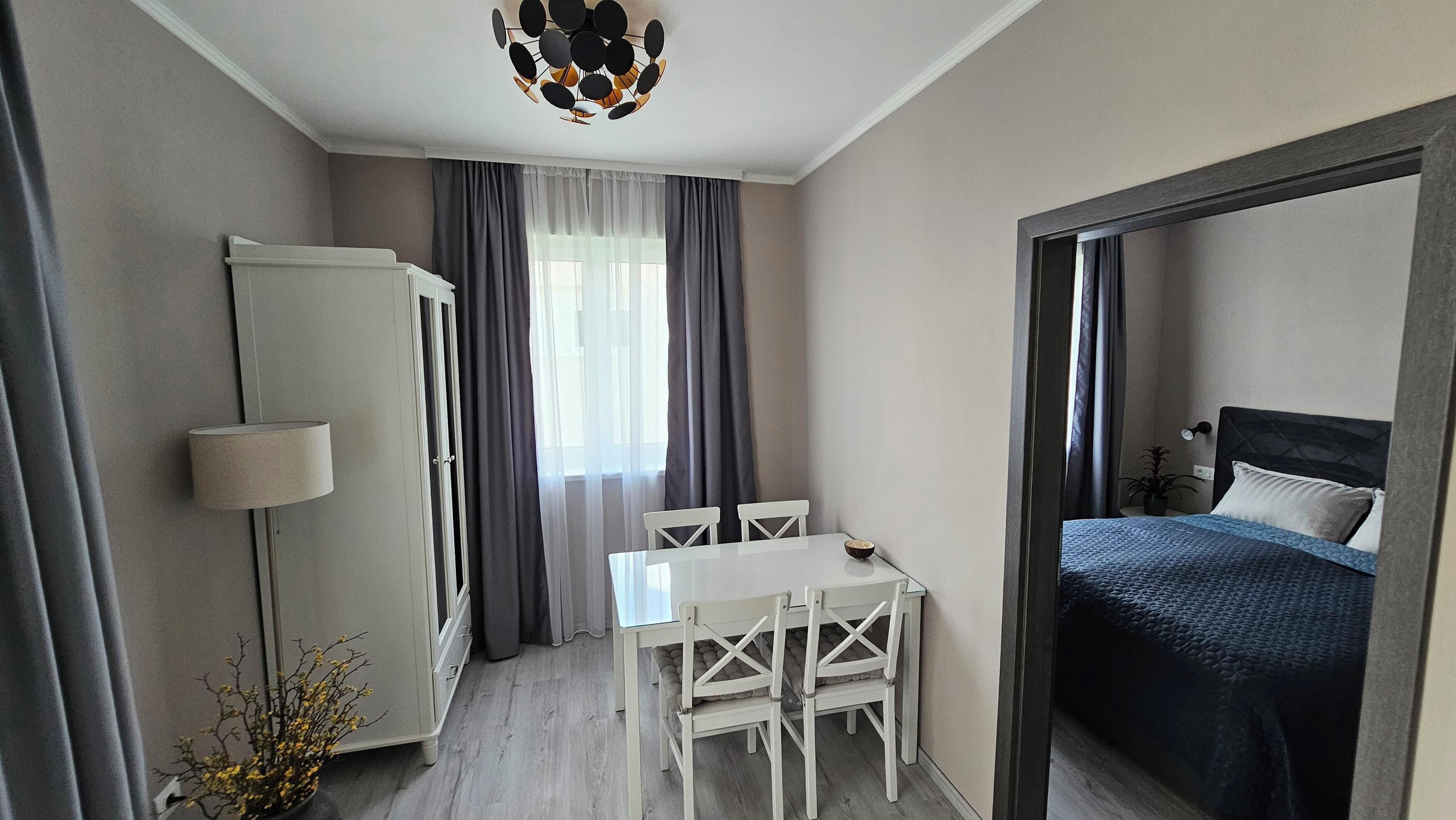 Quarto compacto com cama, uma mesinha com cadeiras, guarda-roupa e luminária no teto.