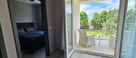 Un dormitorio con cama y balcón que ofrece vistas a zonas verdes y una casa.