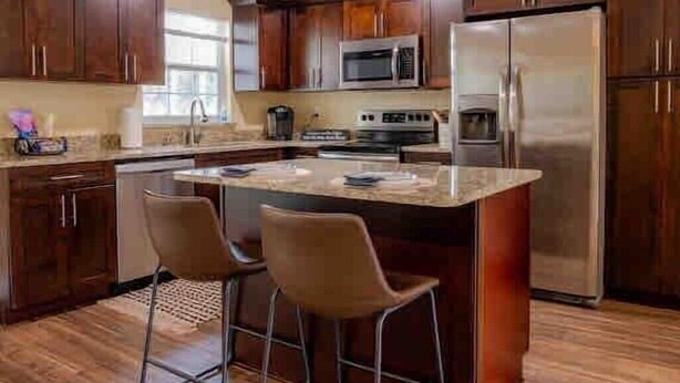 A kitchen with wooden cabinets, a stainless steel refrigerator, a microwave, and a stove. There are two bar stools and a small island with a sink. - 2 separate homes, each 3-bed 2 bath one on Lake and are only a 5-min. car ride. (Lutz)