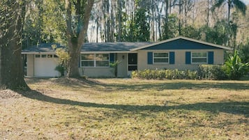 A single-story house with a garage, surrounded by trees and a grassy yard.