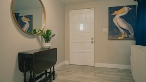 A hallway with a white door, a round mirror, a dark console table with a plant, and a painting of a pelican. - 2 separate homes, each 3-bed 2 bath one on Lake and are only a 5-min. car ride. (Lutz)