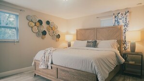 A bedroom with a wooden bed, a wall art piece, two bedside lamps, and a window with blinds. - 2 separate homes, each 3-bed 2 bath one on Lake and are only a 5-min. car ride. (Lutz)