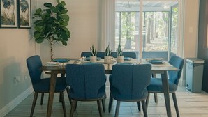 A dining area with a table set for six, surrounded by six blue chairs, a large potted plant, and framed artwork on the wall. - 2 separate homes, each 3-bed 2 bath one on Lake and are only a 5-min. car ride. (Lutz)