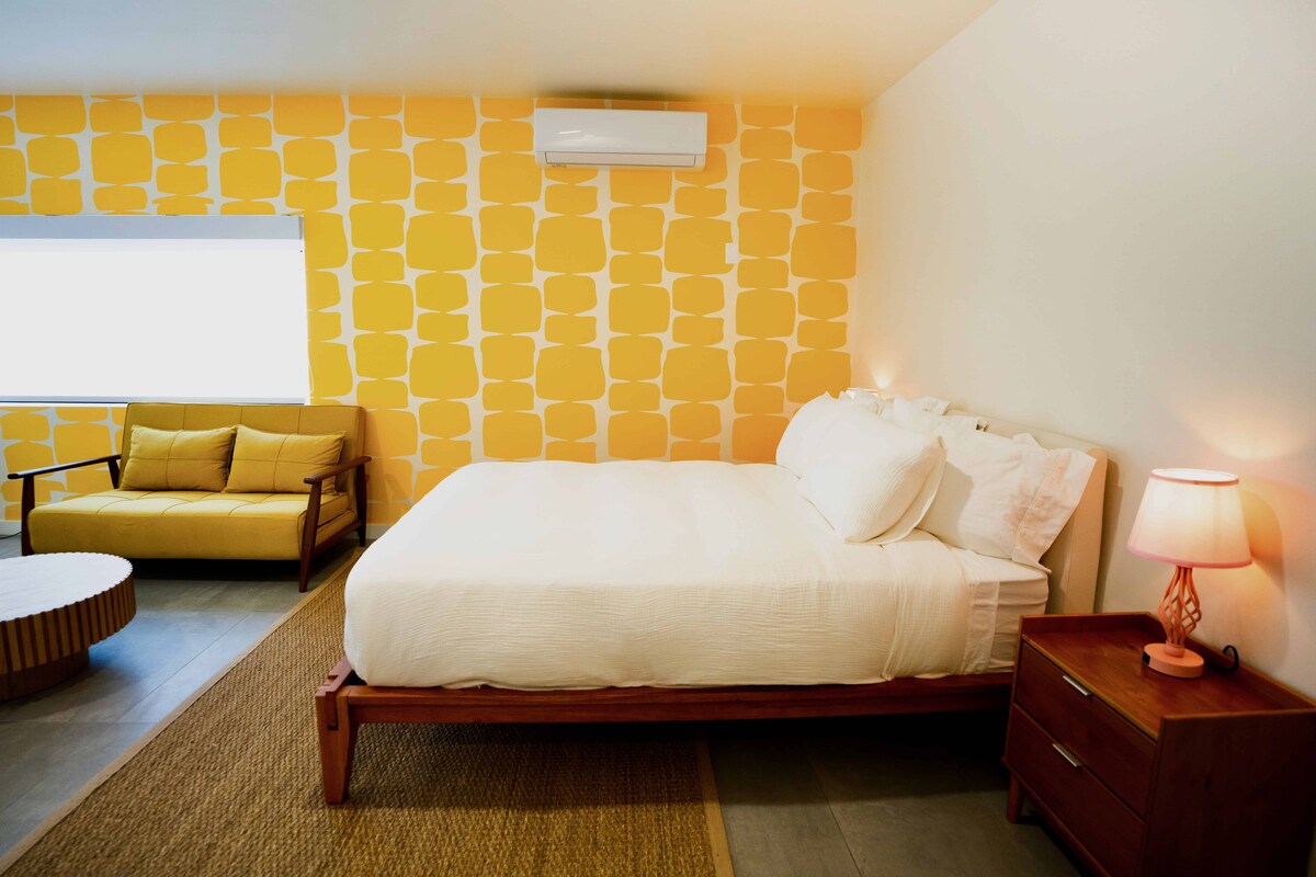 Quarto com cama, mesa de cabeceira, luminária, sofá e parede estampada.