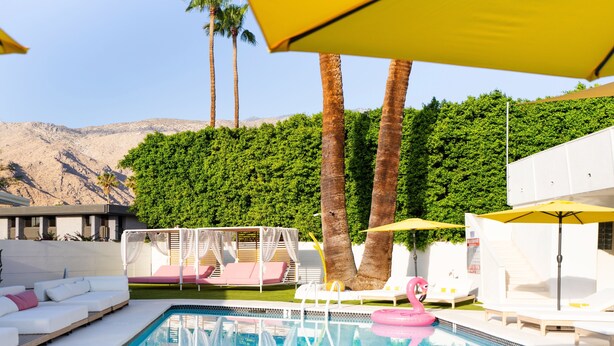 Un espace piscine avec des chaises longues blanches, un flotteur en forme de flamant rose et des parasols jaunes.