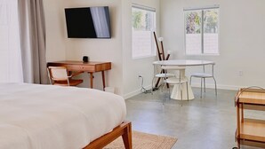 Une chambre à coucher comprenant un lit, un bureau, une télévision et un coin repas avec des chaises et une table.