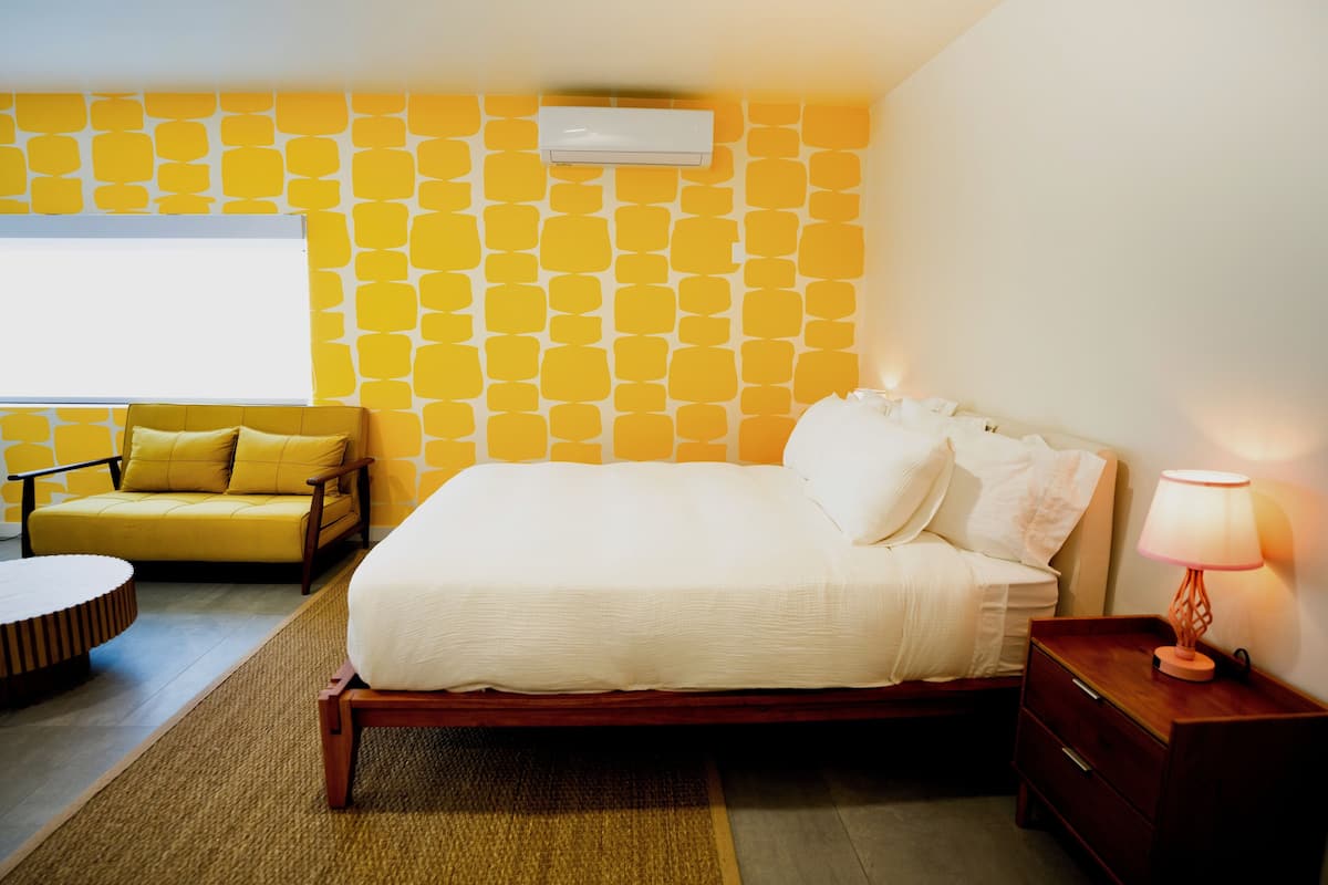 Un dormitorio con cama, mesita de noche, lámpara y pared con un estampado amarillo.