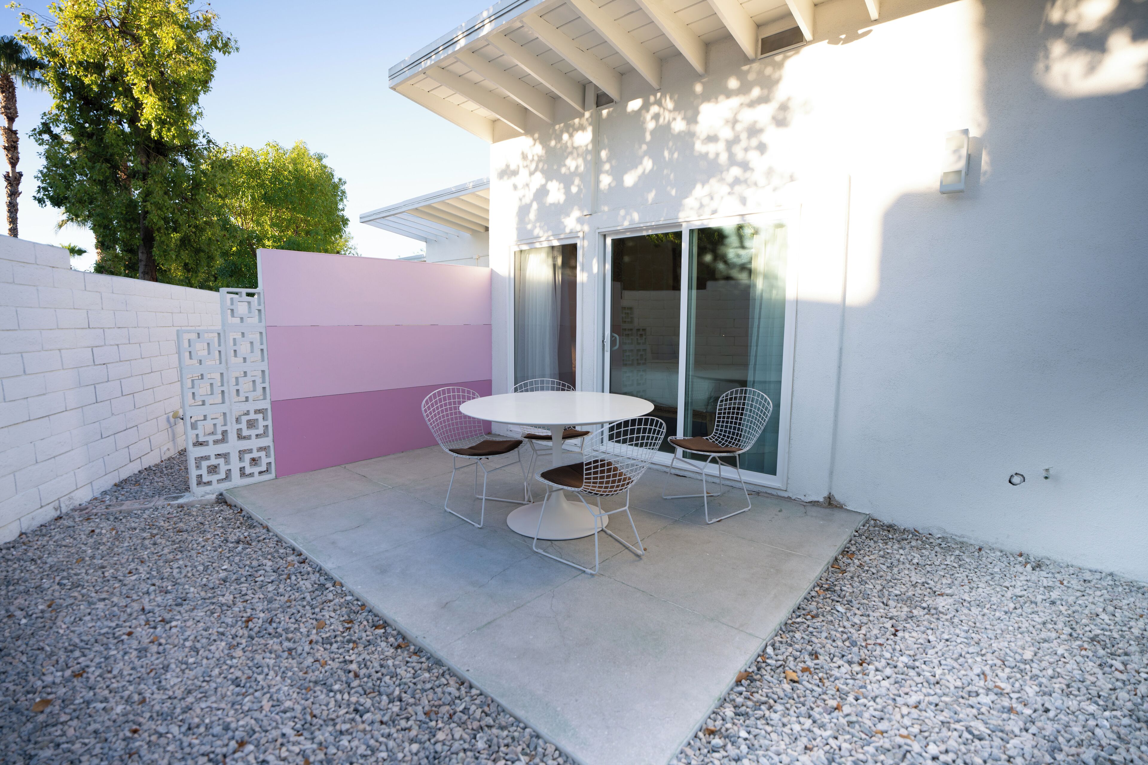 A patio with a round table and four chairs, a white brick wall, and a glass door.