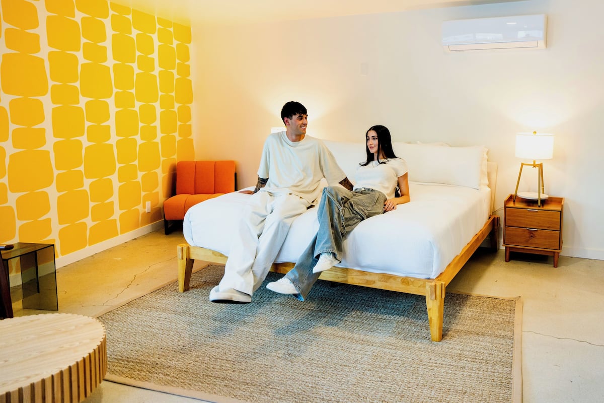 Un dormitorio con cama, mesita de noche, lámpara, silla y pared con diseño geométrico.