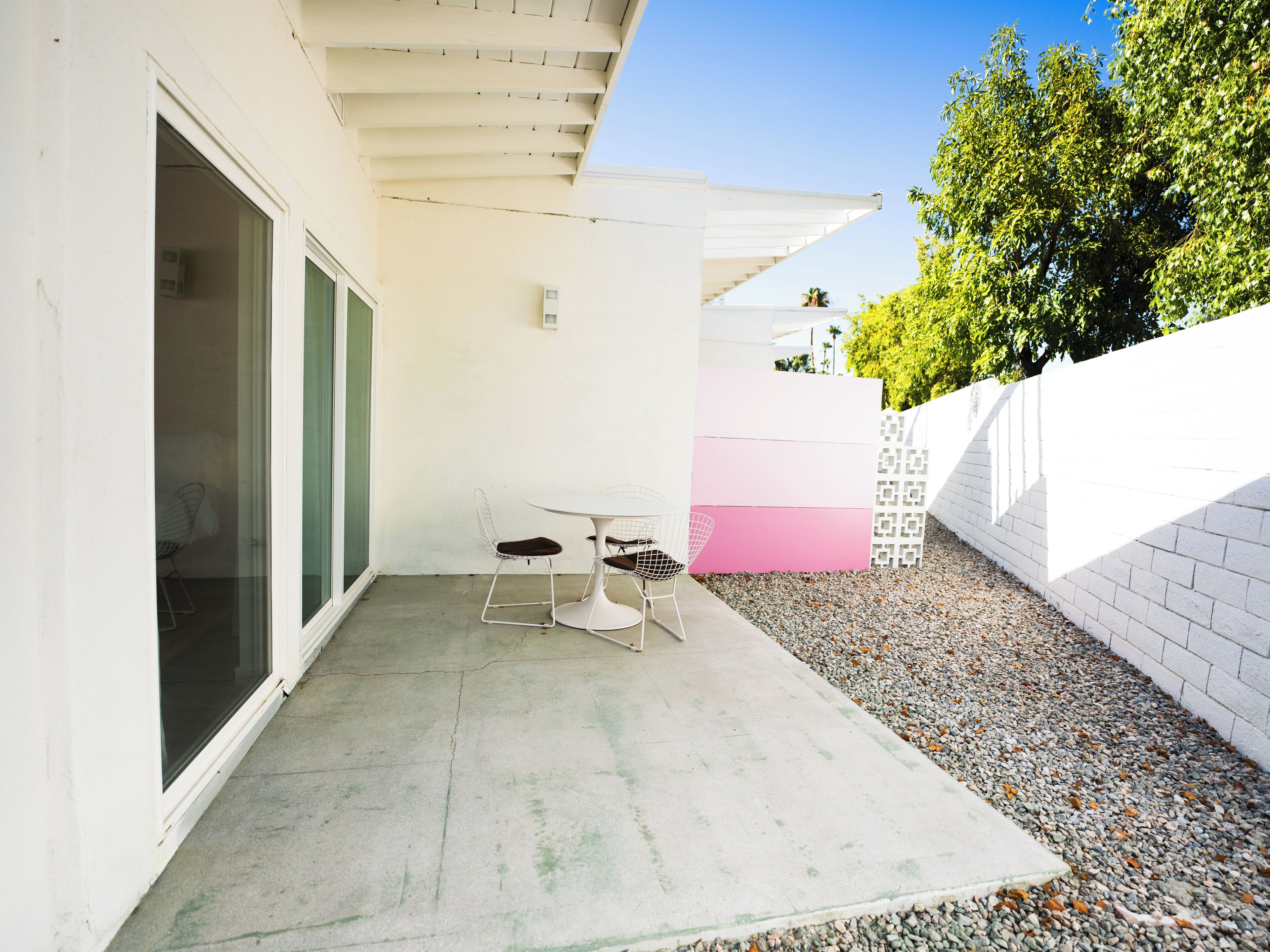 A patio with a table and chairs, a white wall, and a gravel path.