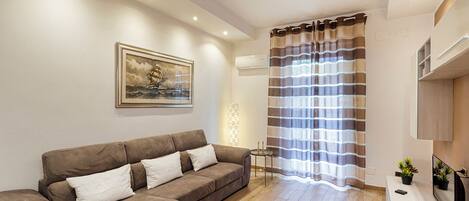 A living room with a brown sofa, a framed picture on the wall, a striped curtain, and a flat-screen TV on a stand.