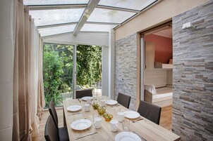 A dining area with a glass ceiling, a wooden table set for four, and a view of greenery outside.