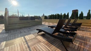 En træterrasse med liggestole og en glasdør, der fører ud til en terrasse.
