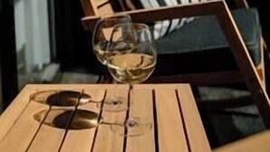 En træstol med pude med striber, et glas hvidvin og et vindue i baggrunden.