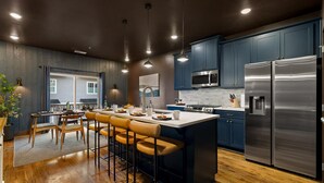 A modern kitchen with dark blue cabinets, stainless steel appliances, and a central island with bar stools. - Southside Speakeasy Townhome, Rooftop Fire Pit (Chattanooga)