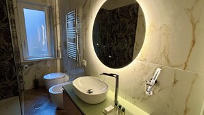 A modern bathroom with a large oval mirror, a round sink, and a toilet.