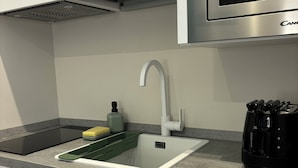 A kitchen with white cabinets, a stainless steel microwave, a sink with a modern faucet, and a black coffee maker.