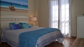 Une chambre à coucher avec un lit, une table de chevet, une lampe et un tableau représentant une scène de plage.