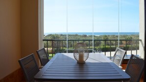 Un balcon avec une table et des chaises, un vase décoratif et une vue sur l’océan et la verdure.