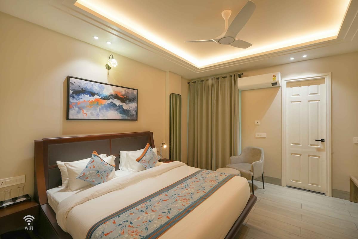 A hotel room with a large bed, a ceiling fan, a painting, a chair, and a door.