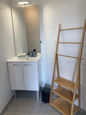Kylpyhuoneessa on valkoinen pesuallas, peili ja kaappeja. Siellä on myös puinen tikapuu ja musta roskakori.