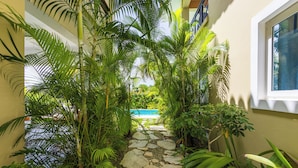 A stone pathway leading to a pool surrounded by lush tropical plants. - Family Elite Golf Vacations in Cocotal (Punta Cana)