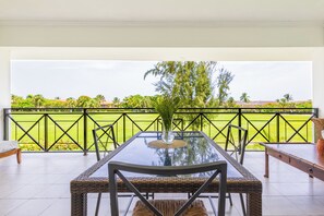A balcony with a glass table, wicker chairs, and a view of a green landscape. - Family Elite Golf Vacations in Cocotal (Punta Cana)