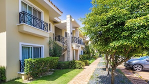 A multi-story hotel with balconies, a paved walkway, and a tree-lined street. - Family Elite Golf Vacations in Cocotal (Punta Cana)