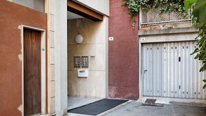 Une ruelle étroite, avec une porte en bois sur la gauche, un portail en métal sur la droite et une petite entrée avec un paillasson.
