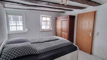 A bedroom with a bed, two windows, a wardrobe, and a door.