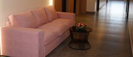 Ein Flur mit einem rosafarbenen Sofa und einem runden Tisch mit Blumen.