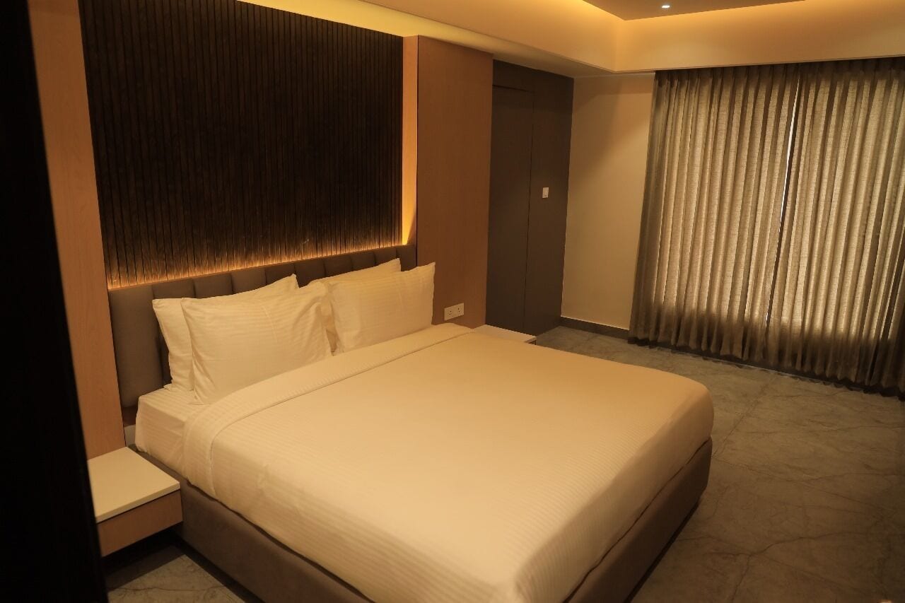 Ein modernes Hotelzimmer mit einem großen Bett, einem Nachttisch, einem Kleiderschrank und einem Fenster mit Vorhängen.