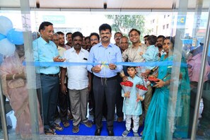 A group of people standing in front of a building with a blue ribbon. - VANTARA SUITES (Vellore)